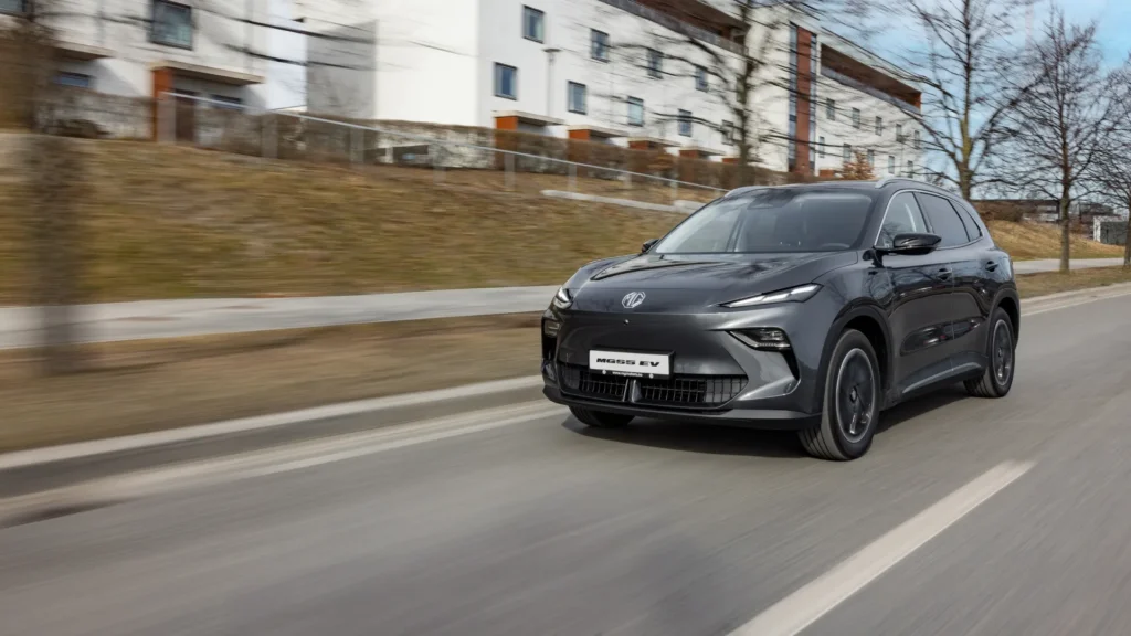 Grå MG el-SUV kjører forbi leiligheter og trær.