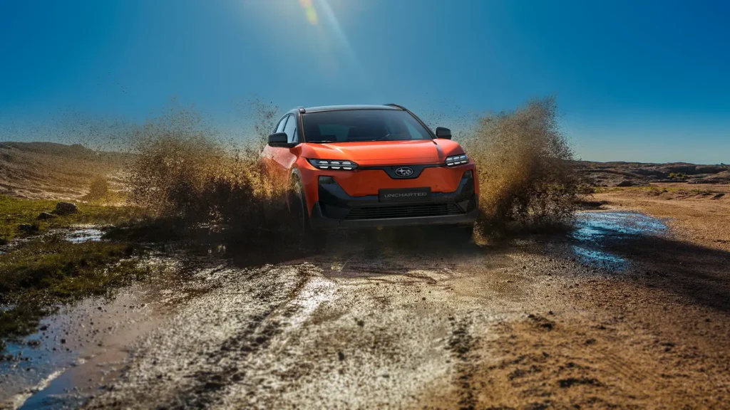 Oransje Subaru SUV kjører gjennom gjørmete vanndam på grusvei.