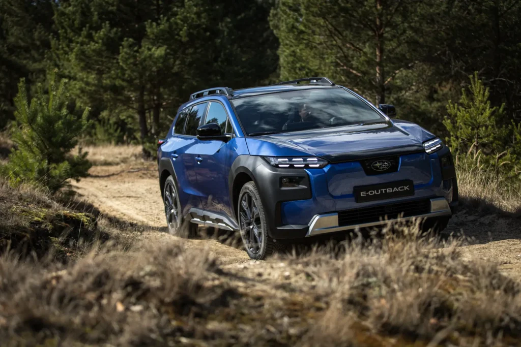 Blå Subaru E-Outback kjører på grusvei i skogsområde.