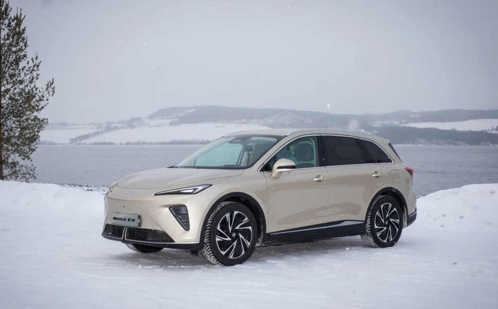 Beige MGS6 på snødekt vei ved innsjø og bakker.